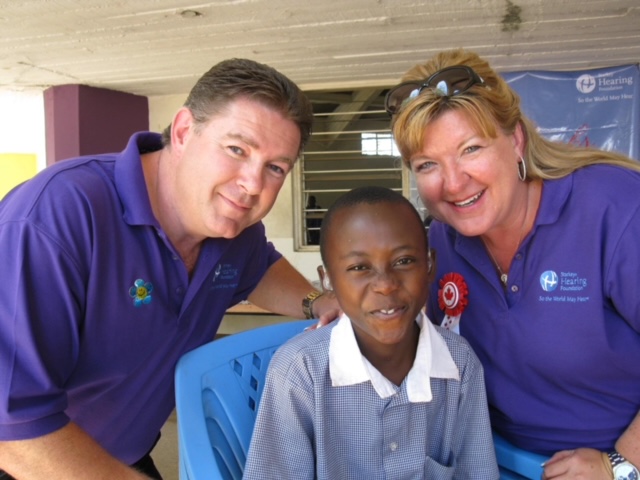 Annette Cross smiling with a teen hearing aid receiver during a giving back mission