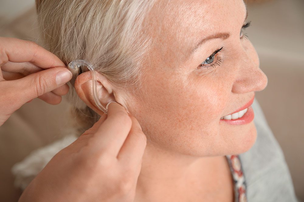 A hearing professional fitting a hearing aid for a lady