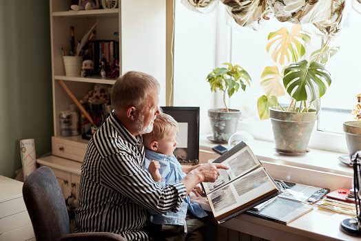 Grandfather and grandson on sofa at home. Grandpa and children looking at old photos